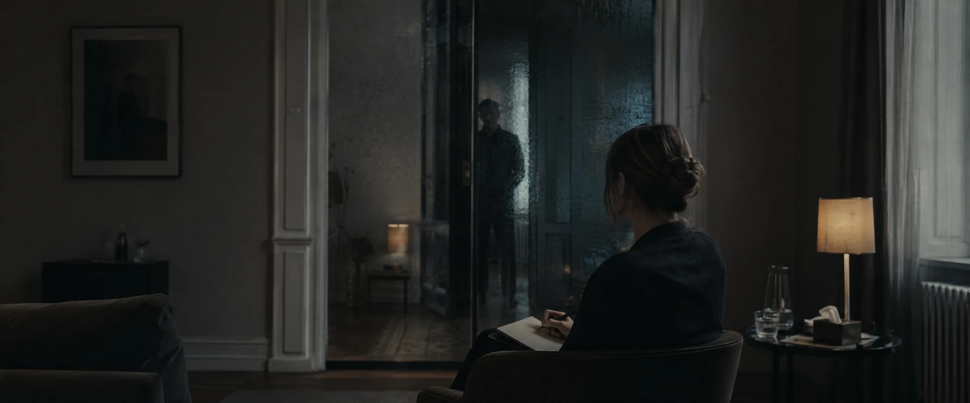 Filmmotiv zu ÜBERTRAGUNG: eine Therapeutin, hinter ihr eine Gestalt im Türglas